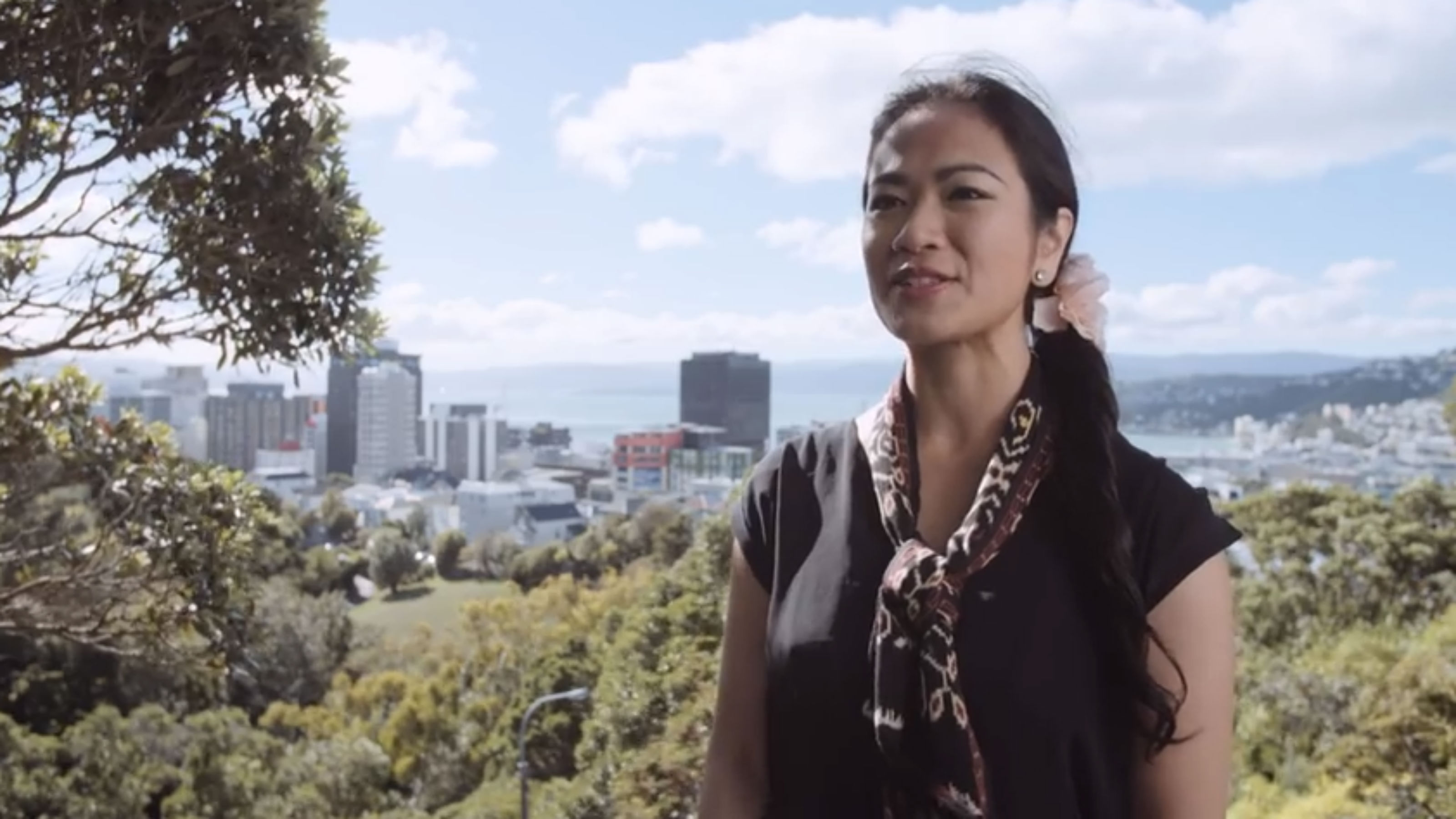 A postgraduate woman stands on a hill with Wellington in the background.