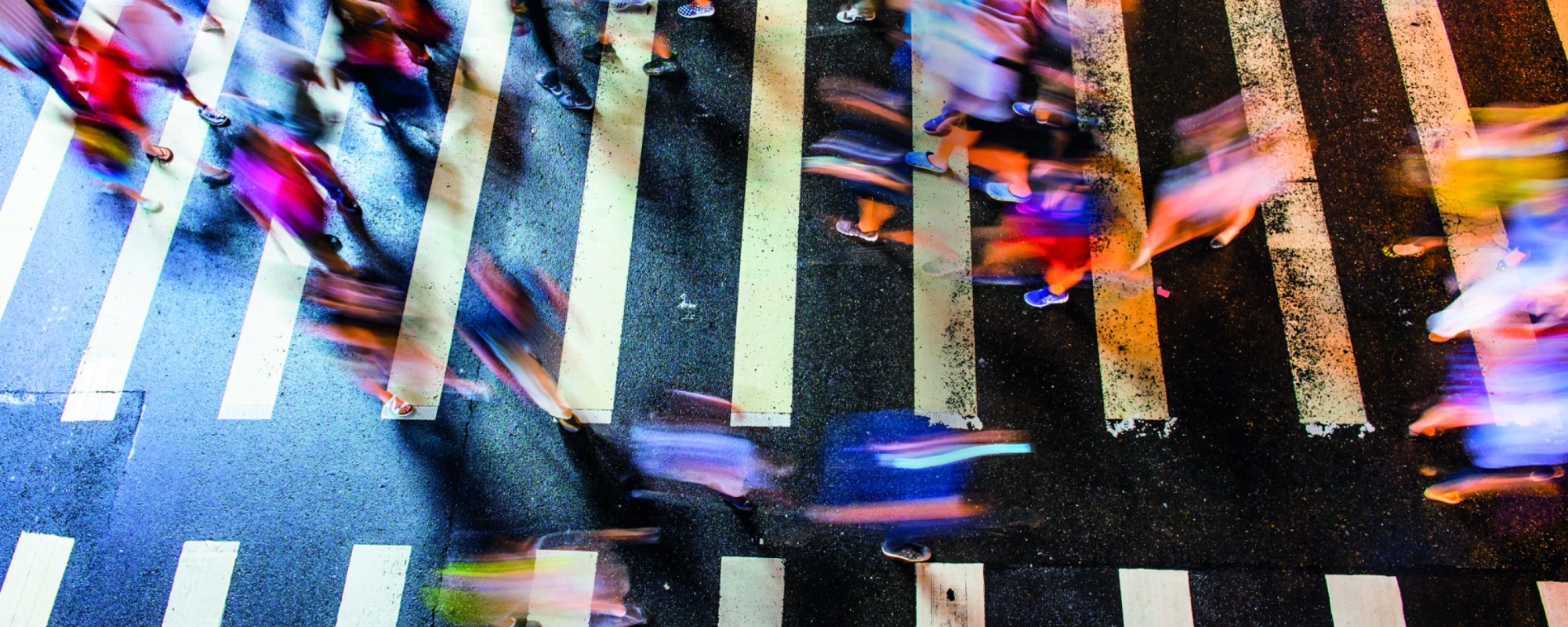 Birds eye view of several blurred people crossing both ways on a zebra crossing.