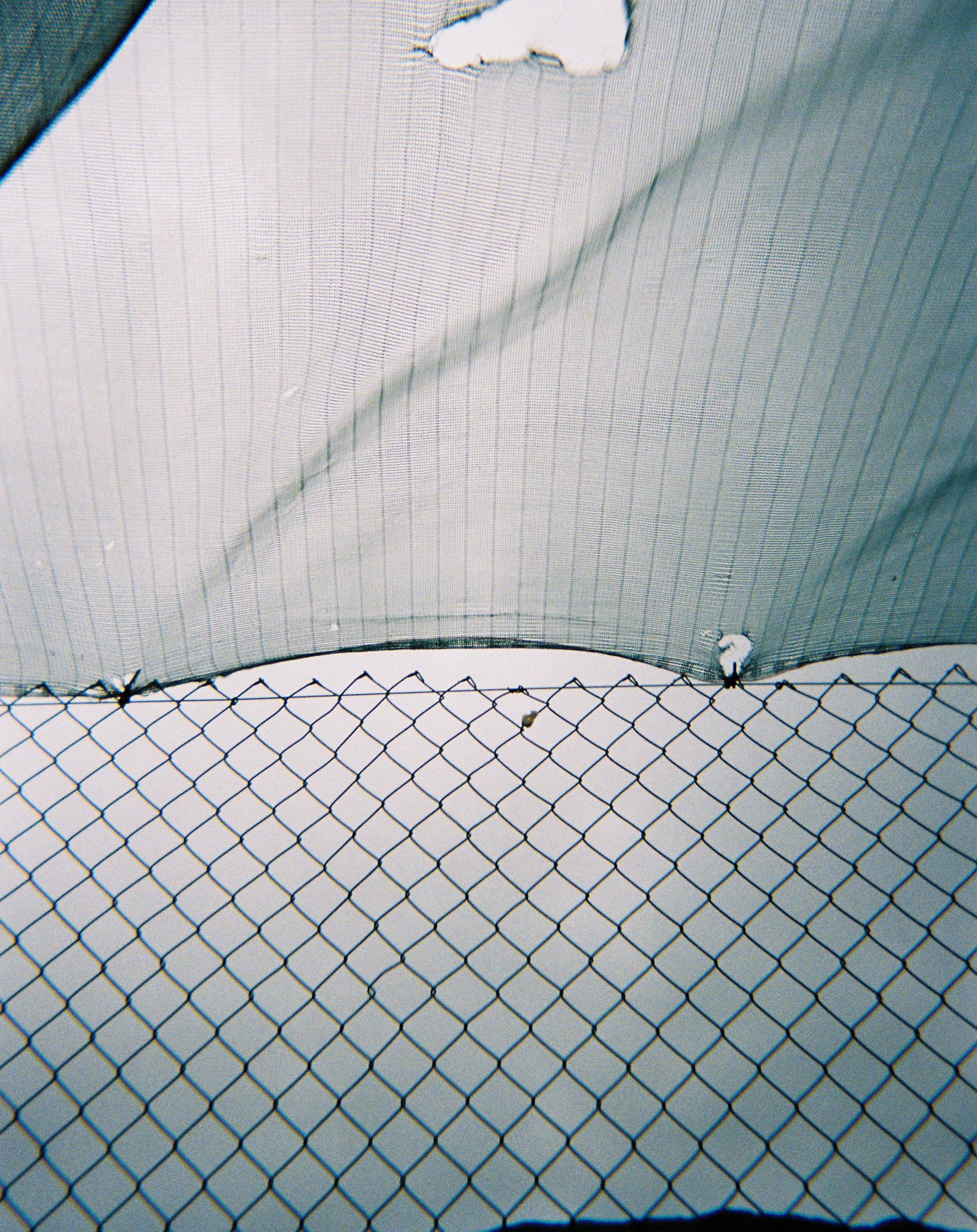 A chain-link fence attached with cable ties to a ripped shade sail.
