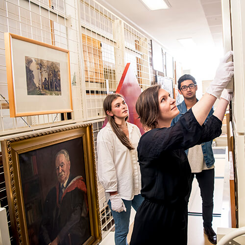 A woman in black clothes with white gloved hands gently adjusting a wall mounted work of art.