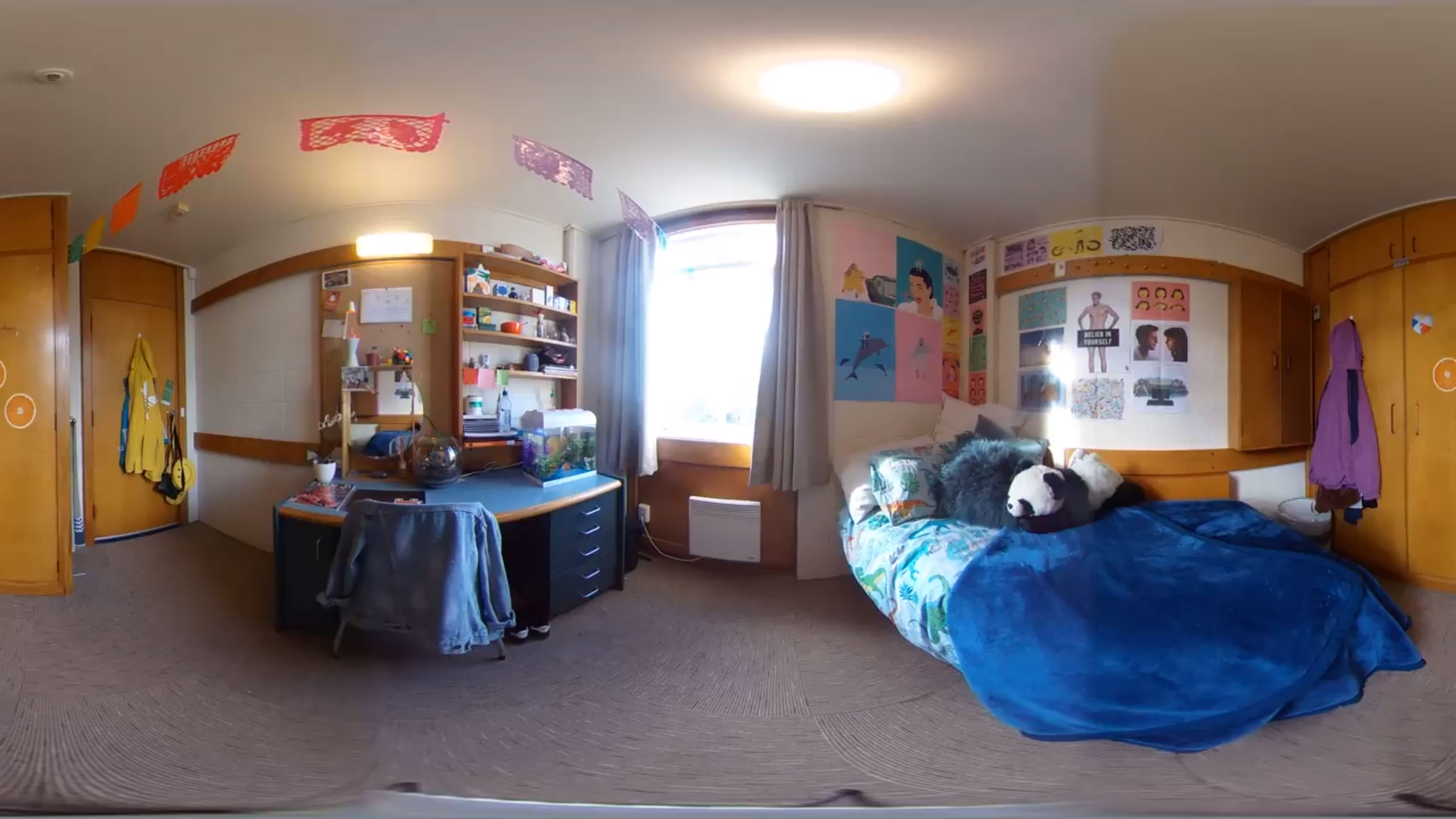 An occupied room with a single bed and desk as well as a fish tank.