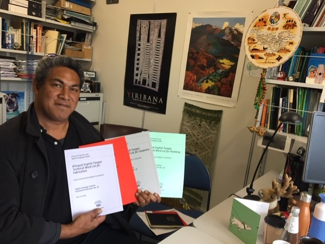 Falakiko (Kiko) Tu'amoheloa sits in his office, holding the booklets in a fan-like manner.