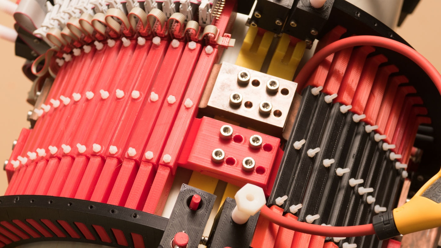 A cylindrical device with many red polymer slats and electronic cables.