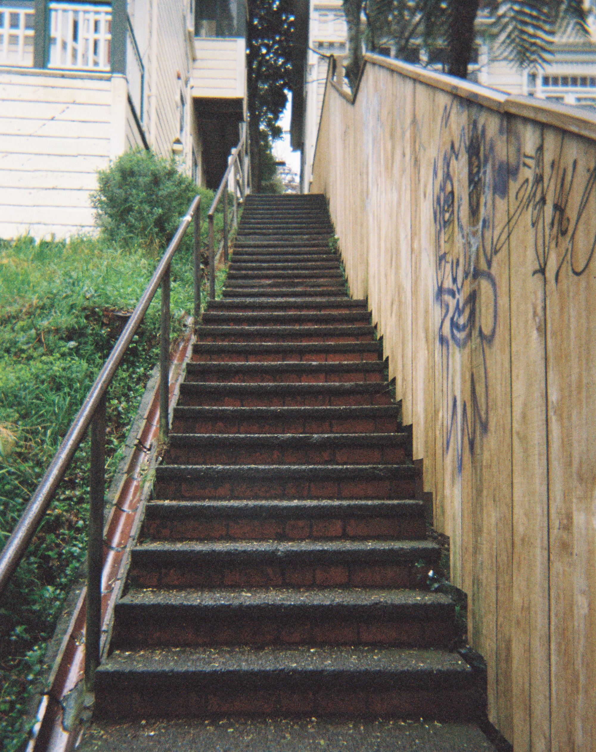 Long set of steps with a rail to the left and a graffitied wooden fence to the right.