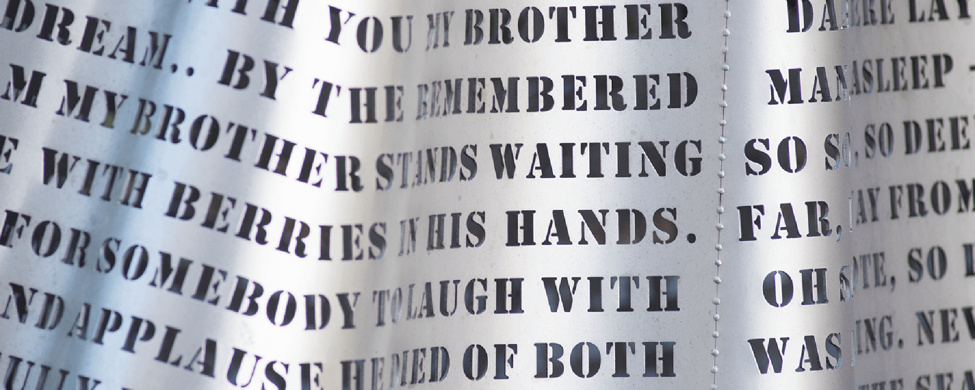 An image of a stainless steel sculpture with many sentances mad up of letters that have been cut out of the steel.