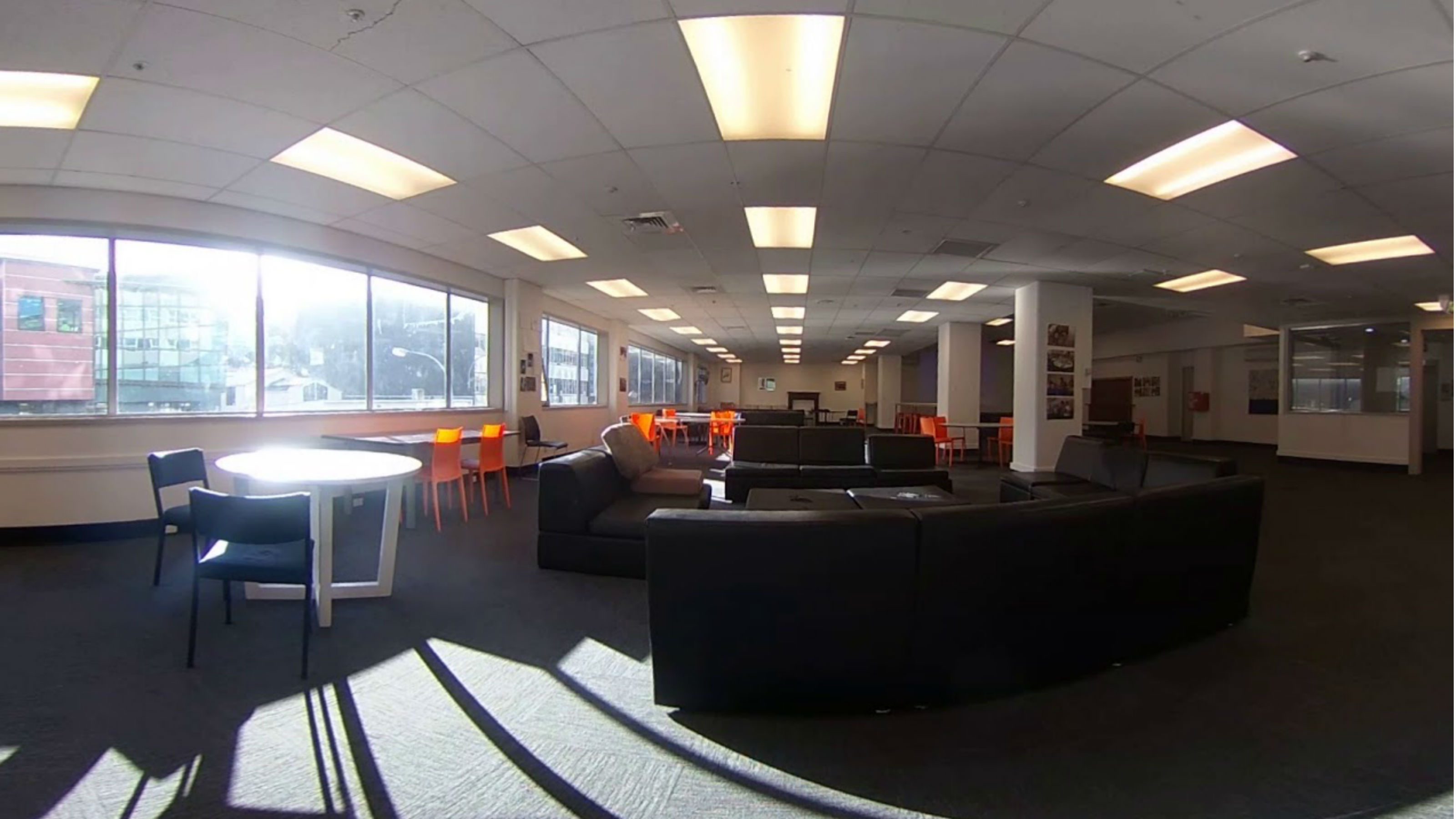 A large common room with black sofas, tables, and chairs.