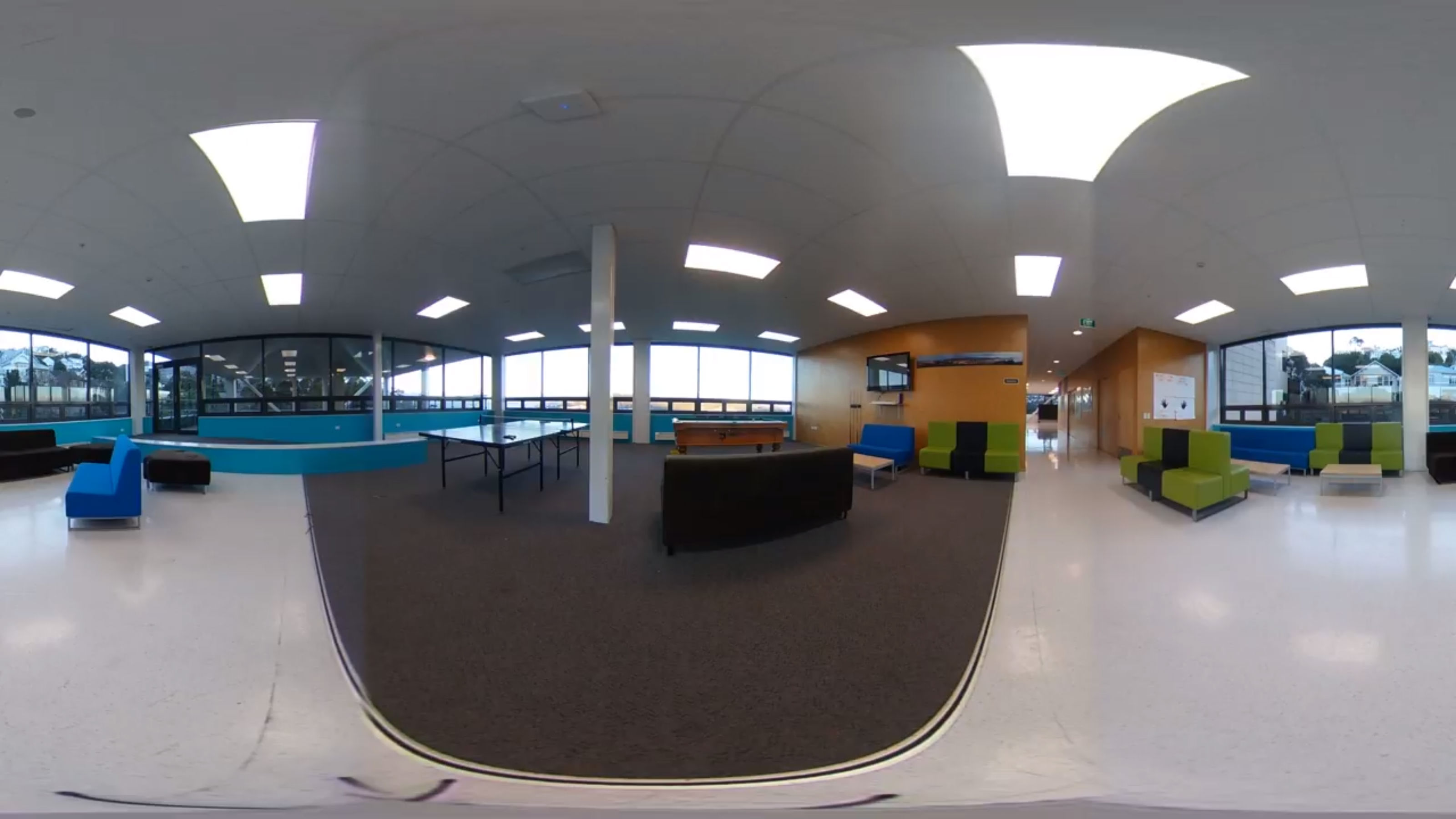 A panoramic view of the common space in Te Puni village with a television, ping pong table, and sofas.