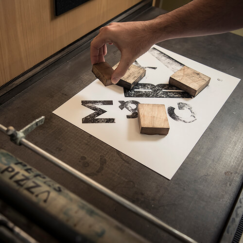 Wooden type blocks making mottled black prints on flat white card.