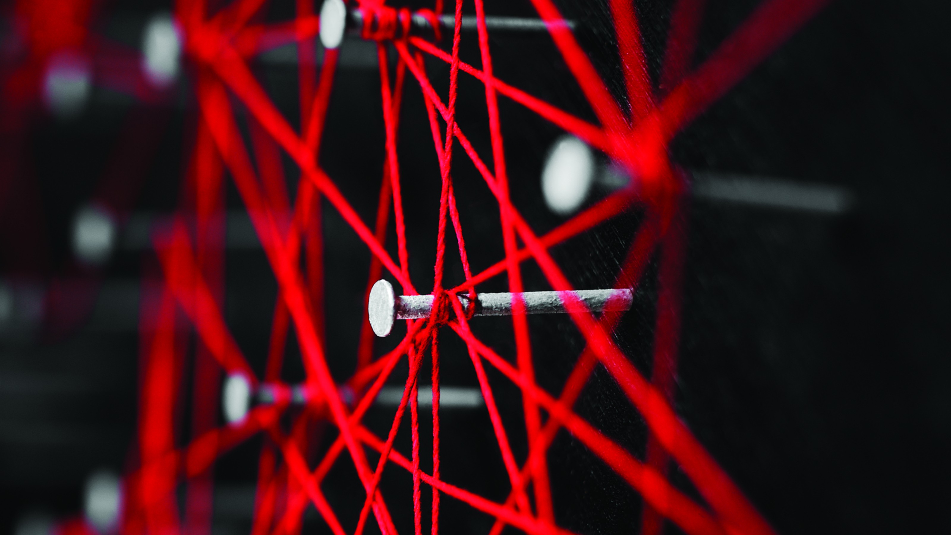 An image of red strings tied around nail heads set against a black background.