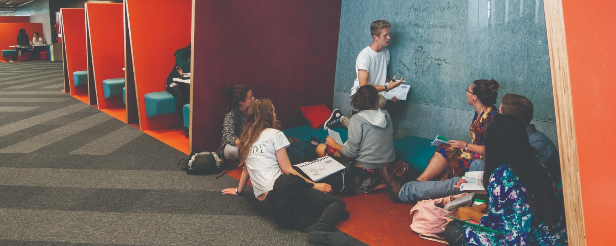Group of seven students gathered around a whiteboard, one of whom is writing on the board.