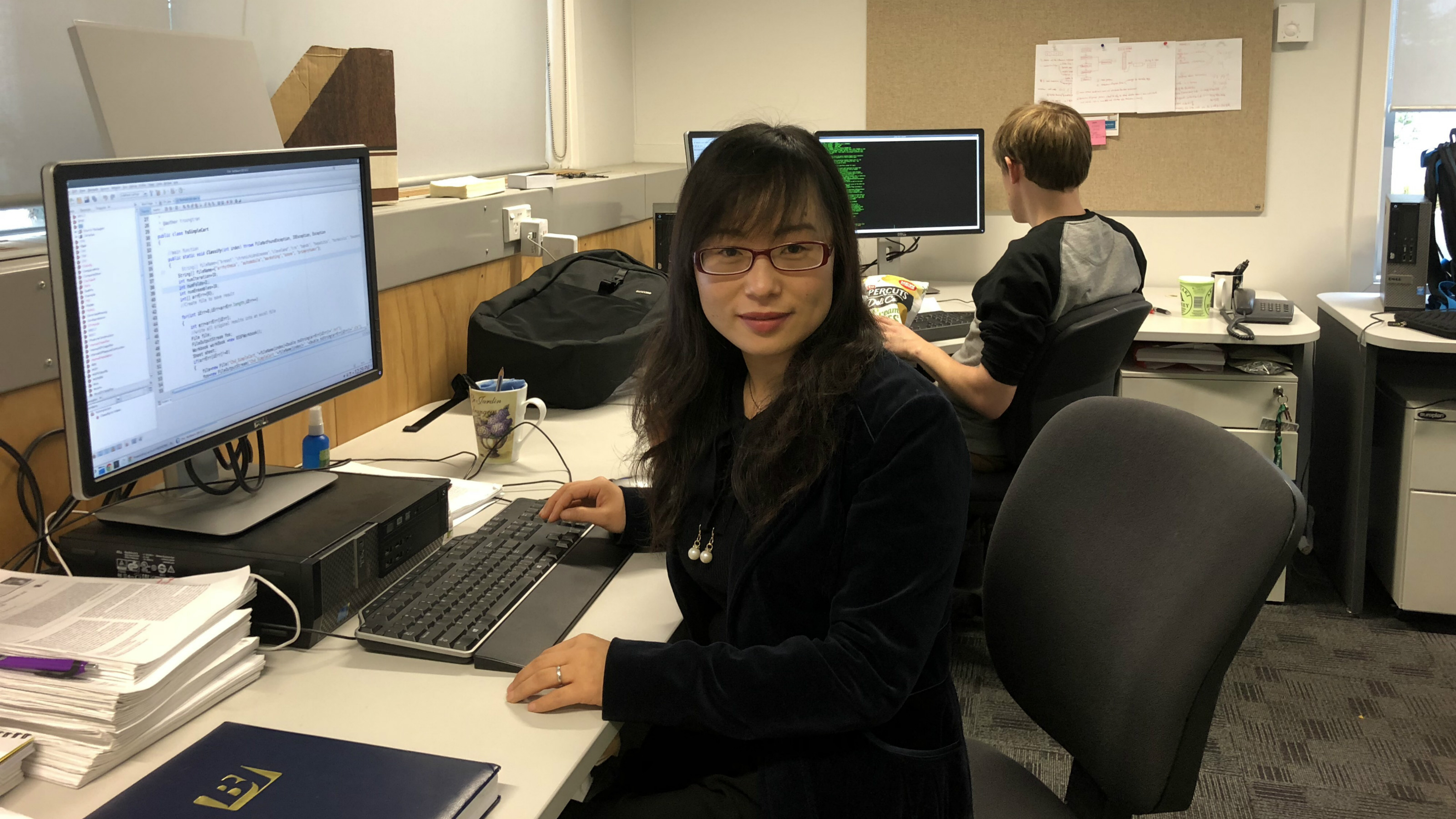 Dr Bing Xue sits at a computer in an office
