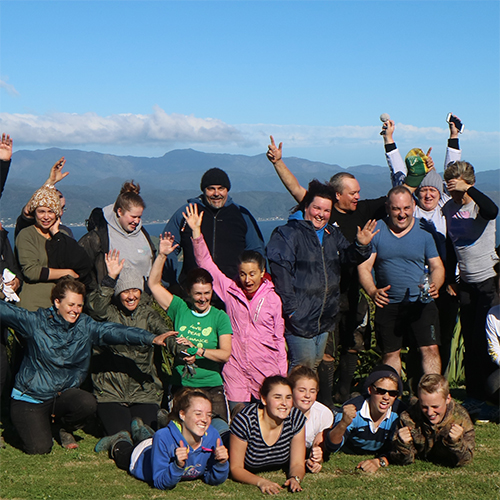Participants smile and wave during a group photo taken on a patch of grass following the Wellington Corporate Challenge.