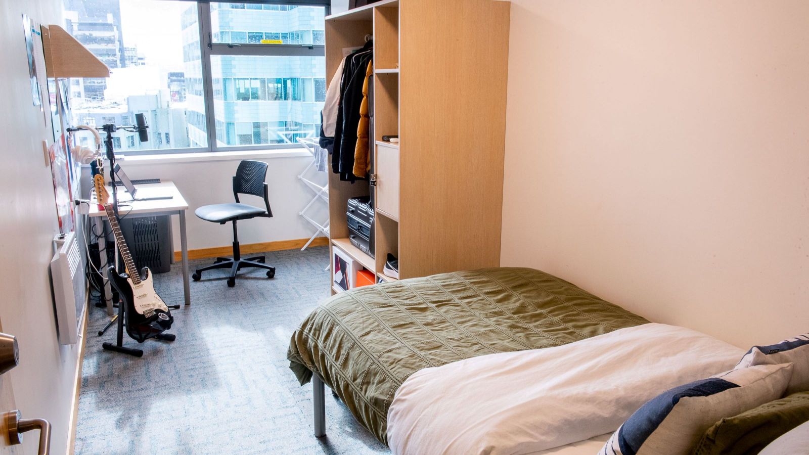 Single room with a bed, wardrobe and shelving unit, and desk.