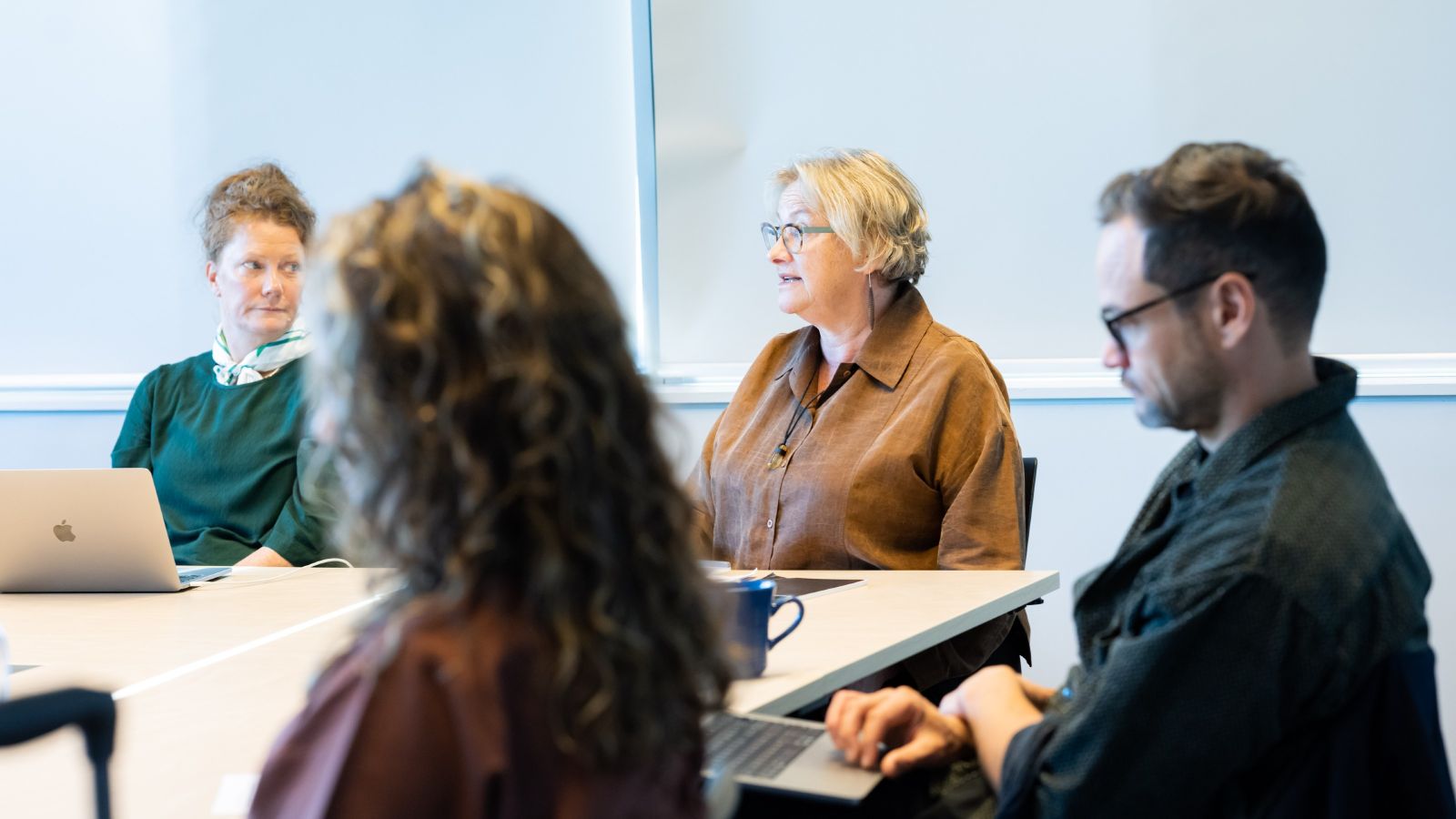 Four academics sat at a table discussing, two are in focus, and two are out of focus in the foreground.