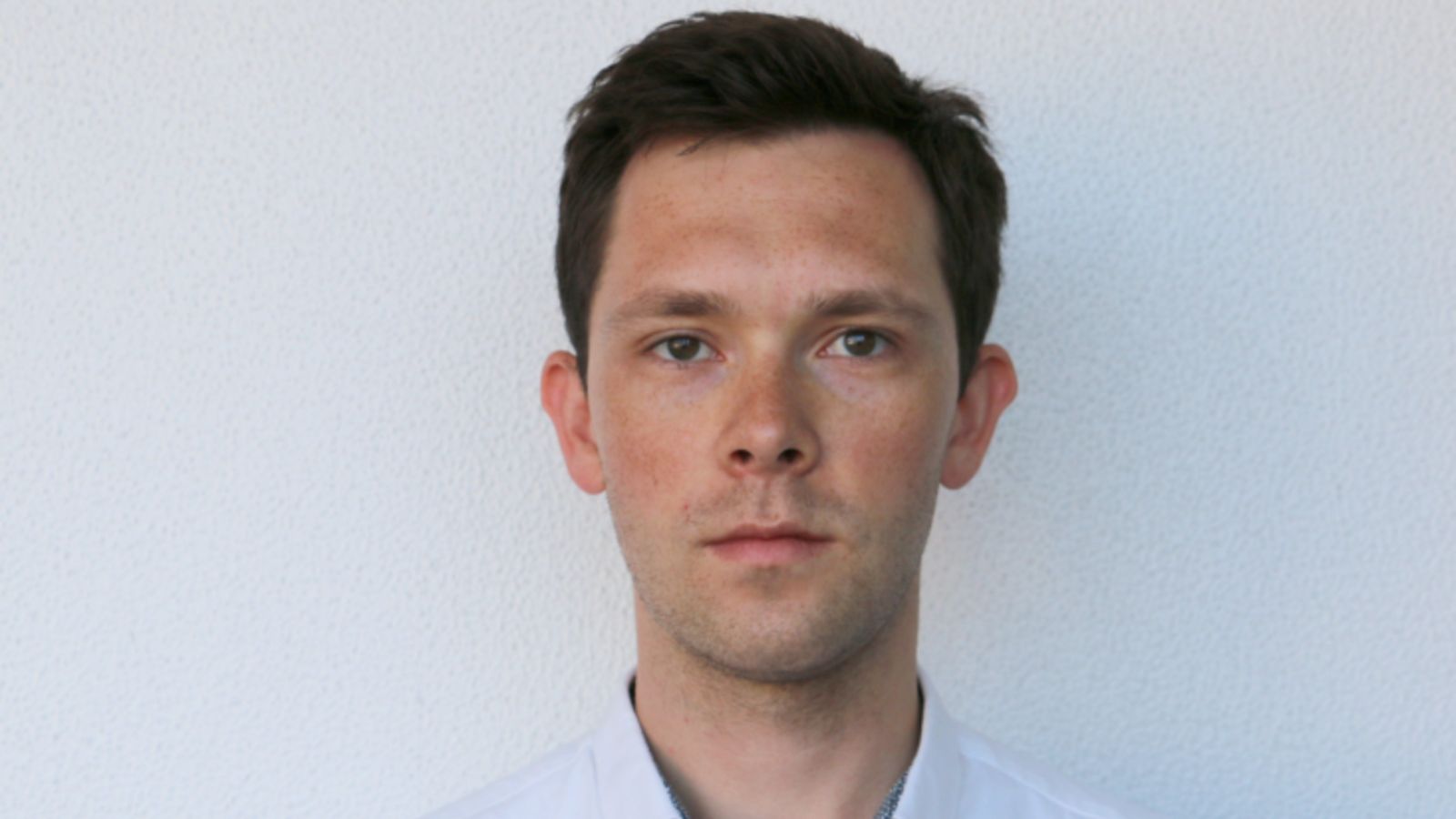 Portrait of Tom Coad facing the camera. Tom has brown hair and wears a light-coloured collared shirt.