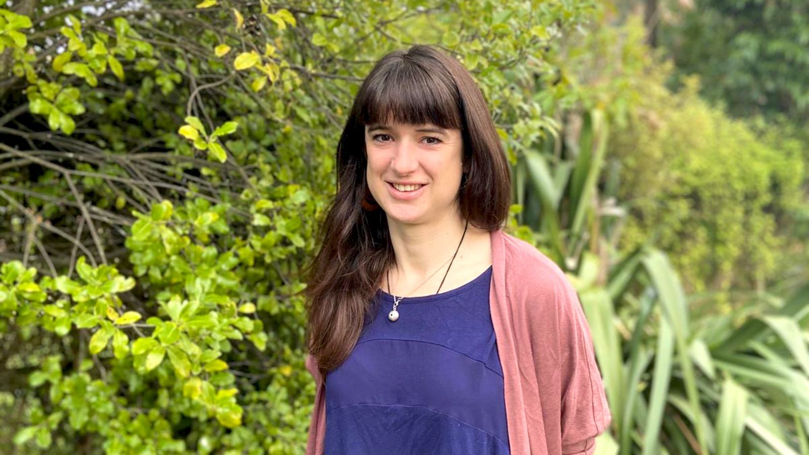 Head and shoulders photo of Kate standing in front of greenery