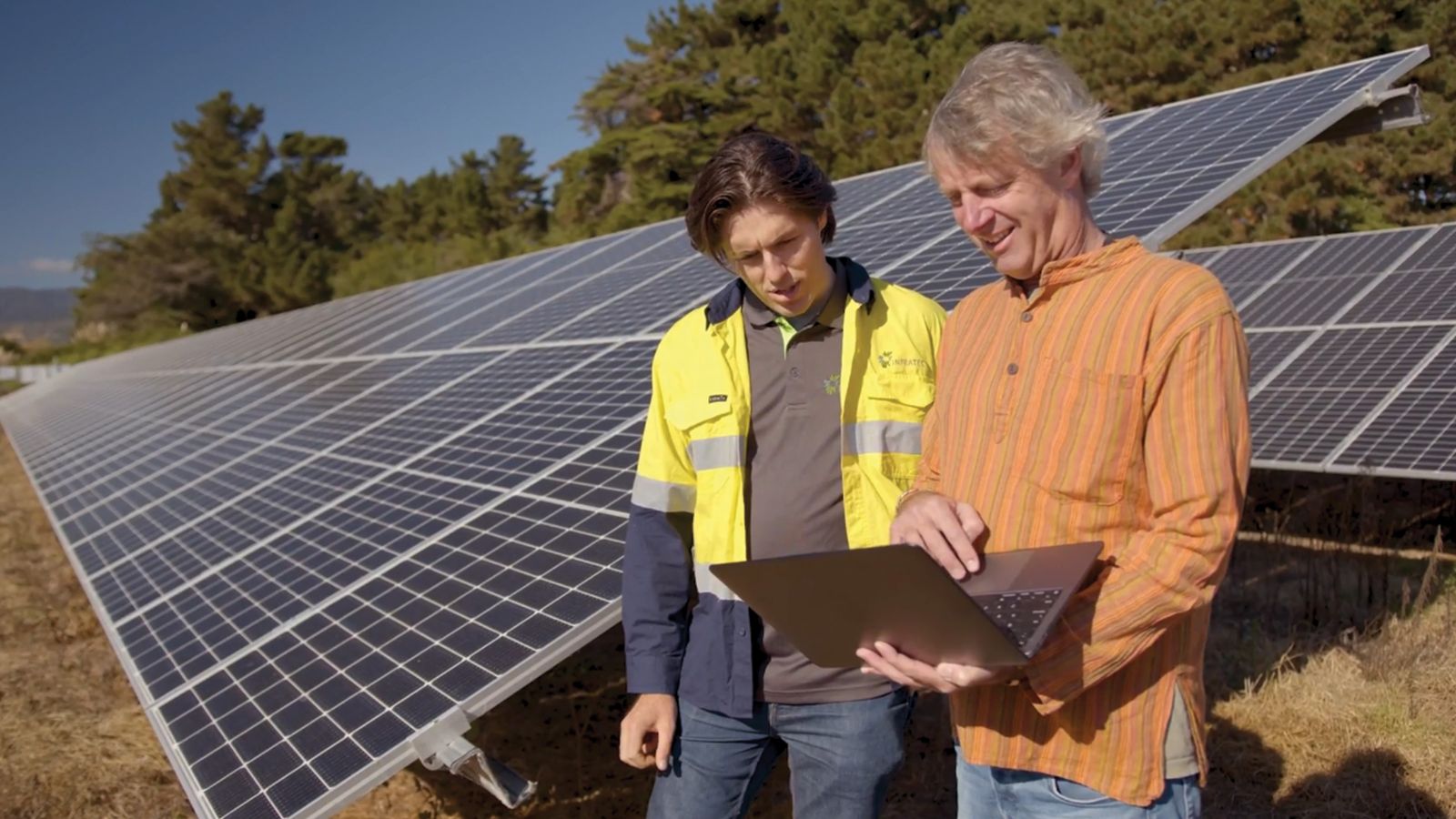 Two men looking at a laptop in front of solar panels