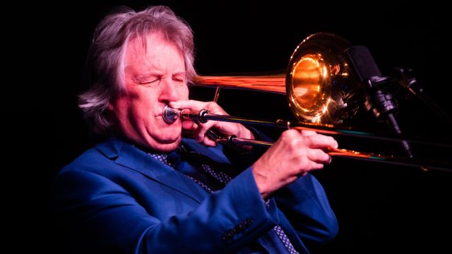 A man in a blue suit is playing the trombone.