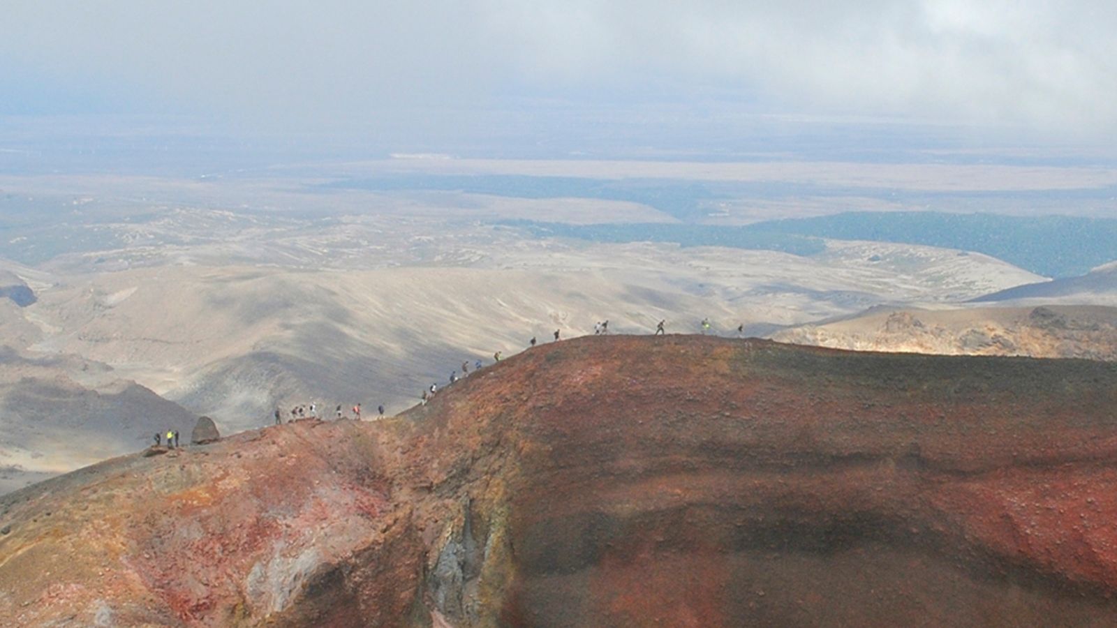 Distant aerial view of people hiking along ridge of brown mountain