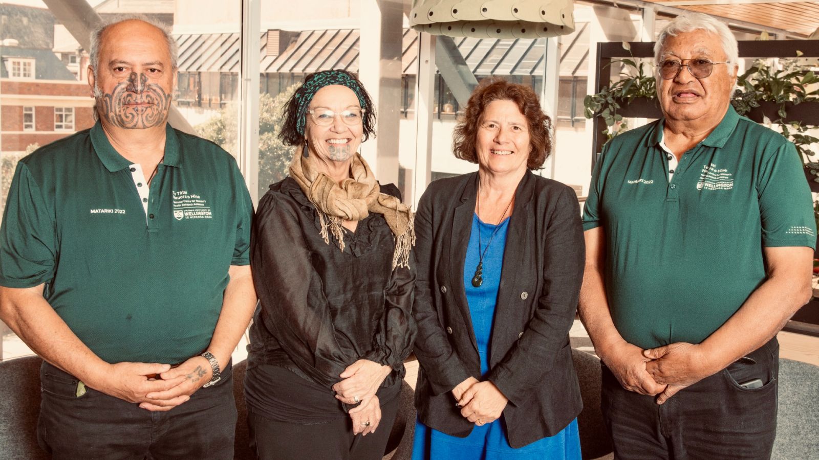 bev-awards Group in smart casual attire stands in front of window, framed by decorative lights and lush plant wall, creating a stylish natural backdrop.