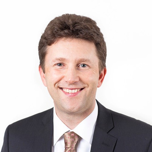 Man with brown hair wearing a suit and tie smiling