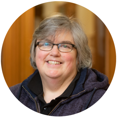 Woman with grey short hair and glasses smiling.