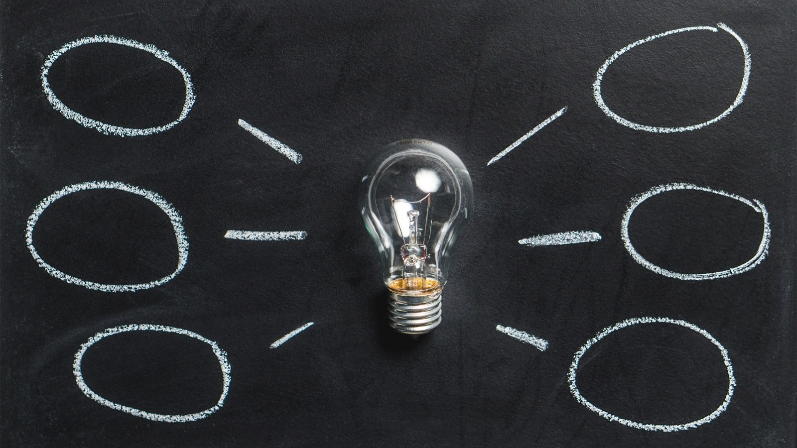 A light bulb positioned on a chalk board. Speech bubbles are drawn around the lightbulb in chalk.
