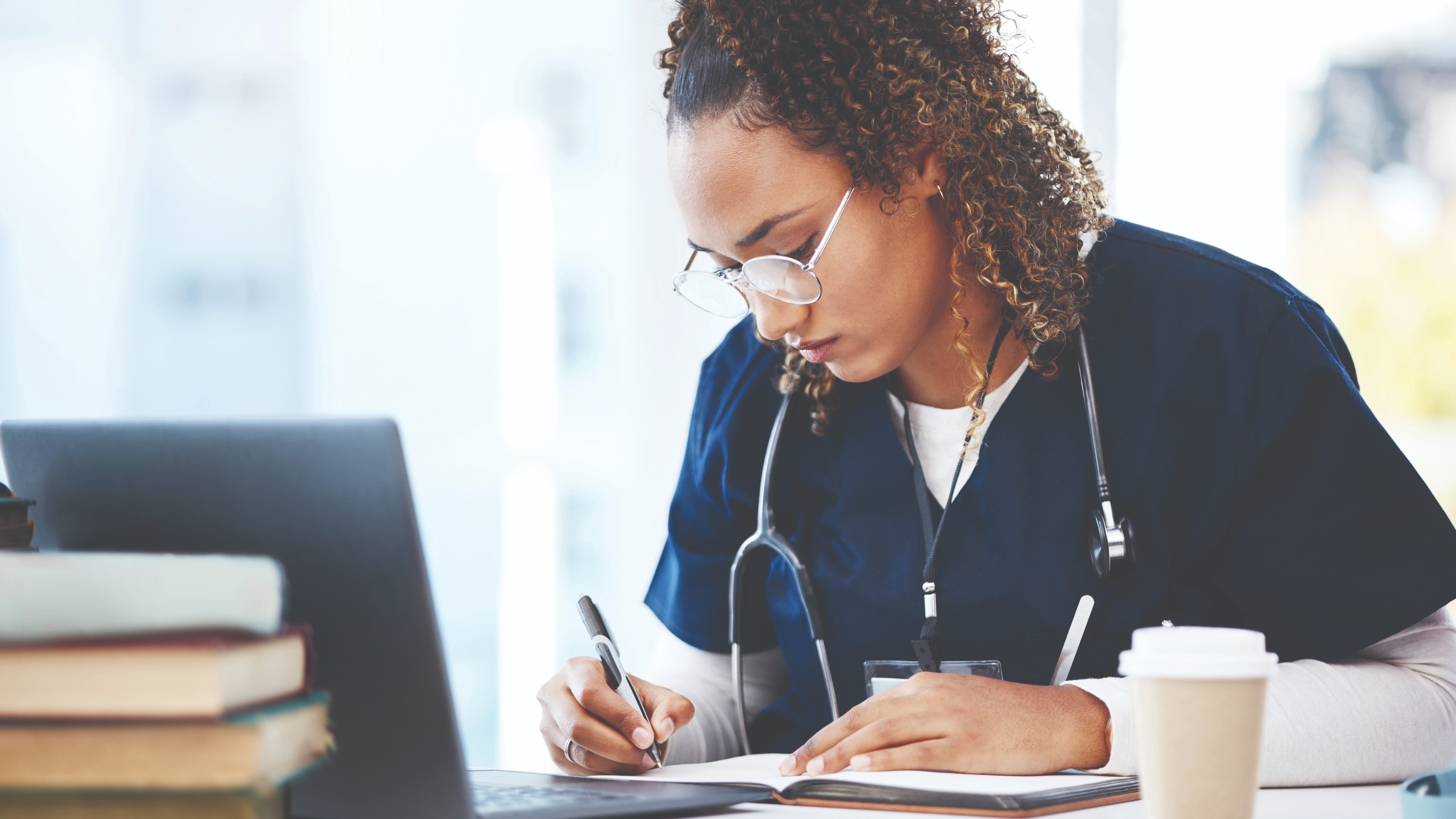 Woman with glasses and stethoscope writes in journal