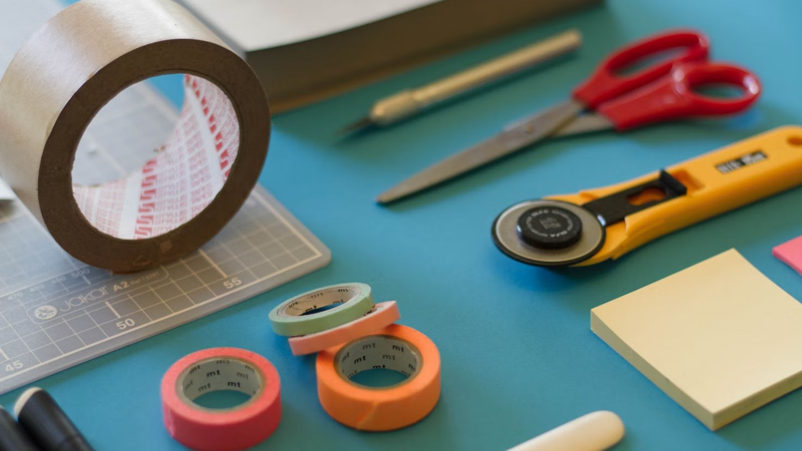 Assorted crafting materials like tape, pen, scissors and a craft knife on a table